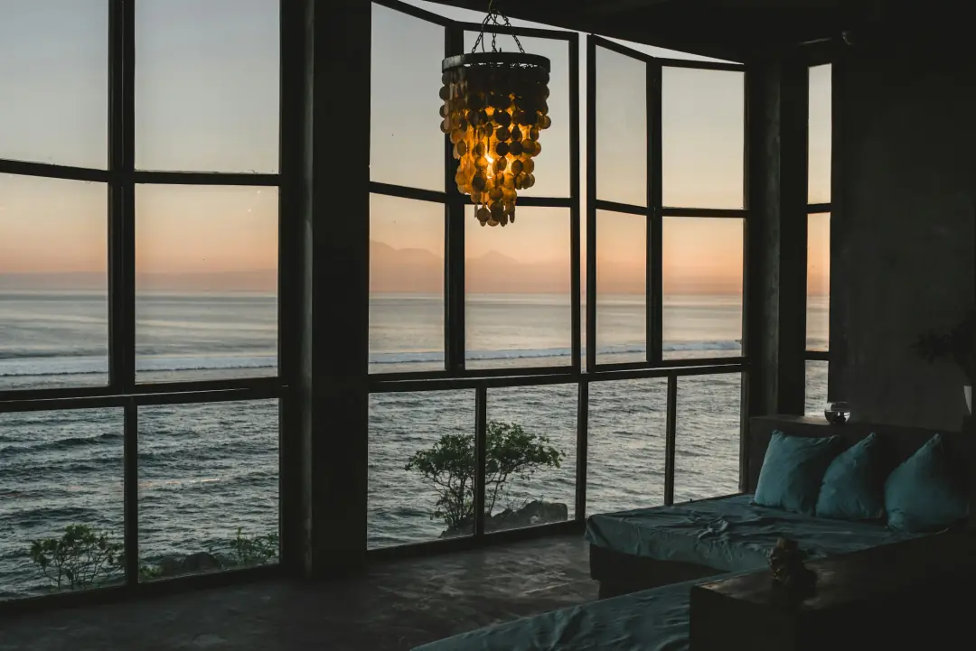 A living room with a wall of windows facing the ocean at sunset