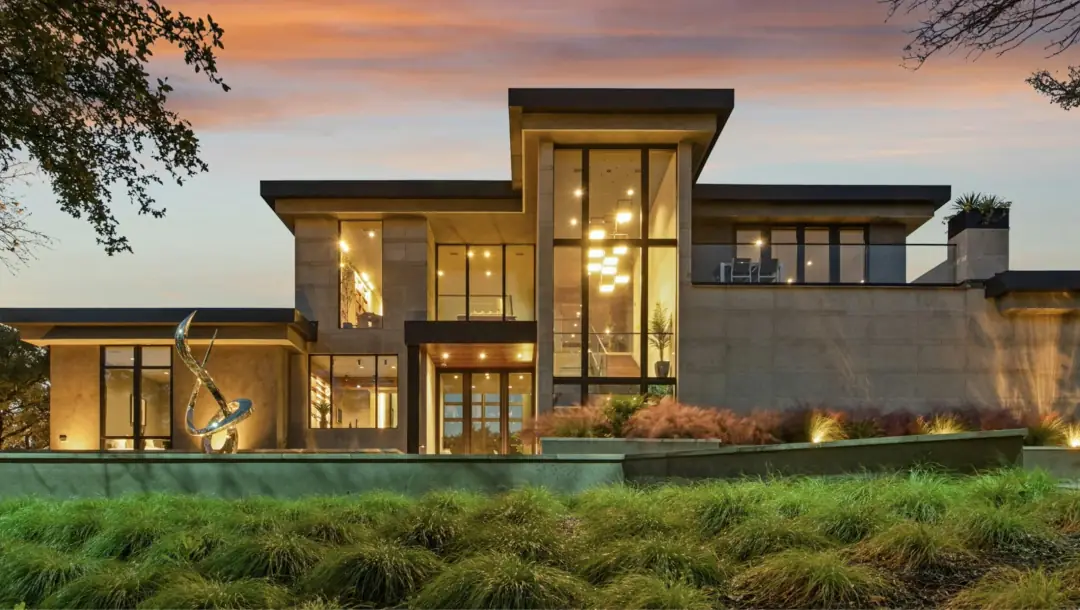 A modern residence with tall glass, lit from within at dusk